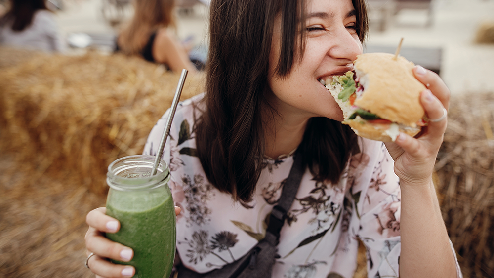 Person som spiser sandwich og drikker grønn juice 